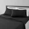 A black microfiber flat fitted sheet set with white pillowcases is displayed on a bed.