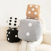 A stack of plush dice cube cushions in beige, gray, and brown with white polka dots.
