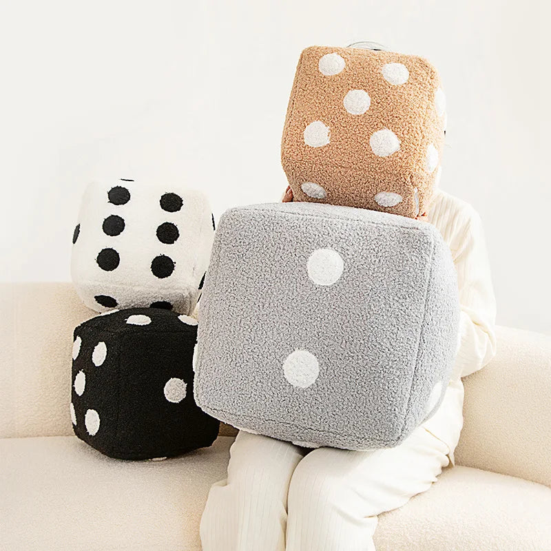 A stack of plush dice cube cushions in beige, gray, and brown with white polka dots.