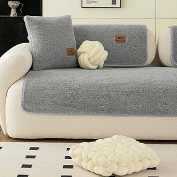 A light gray sofa with matching throw pillows and a white knitted decorative object on the floor.