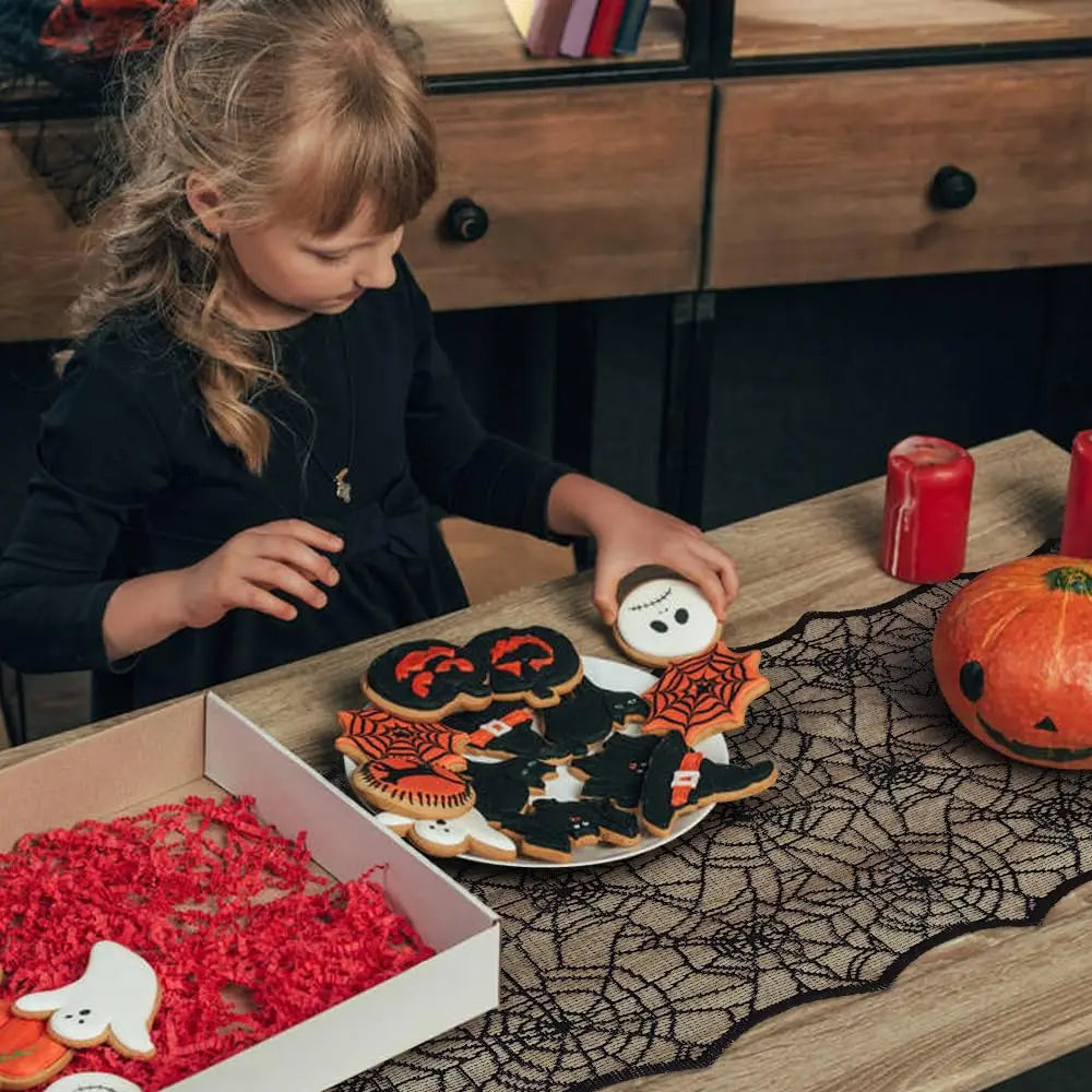 Spider web black lace table runner for Halloween featuring orange and black decorative items.