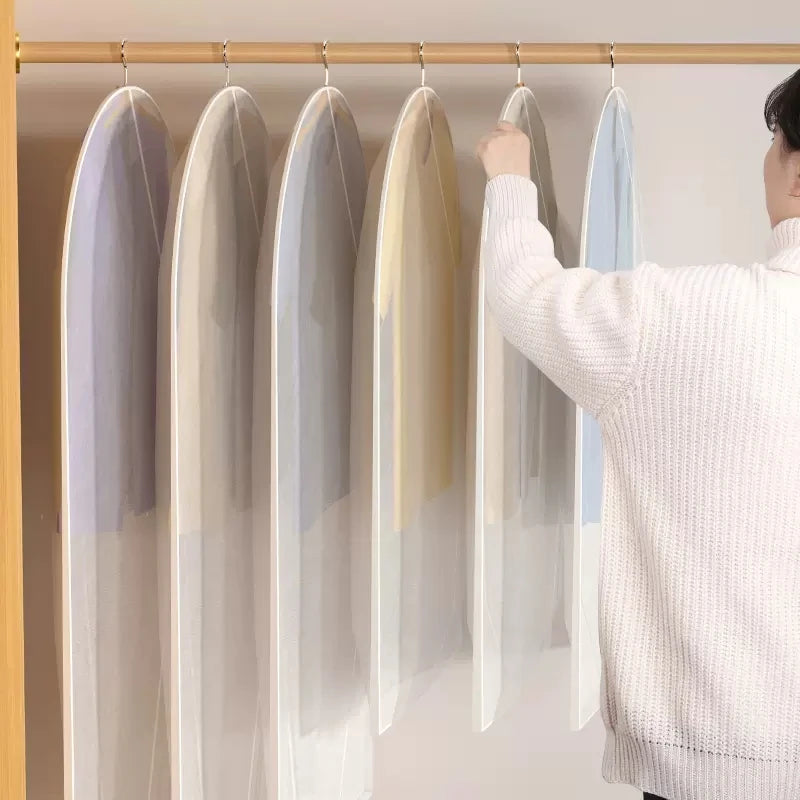 A person is hanging a transparent zippered clothes storage bag on a wooden rack.