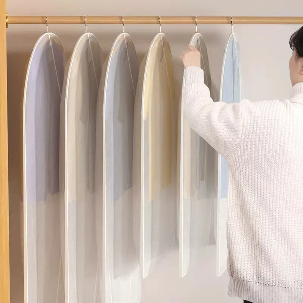 A person is hanging a transparent zippered clothes storage bag on a wooden rack.