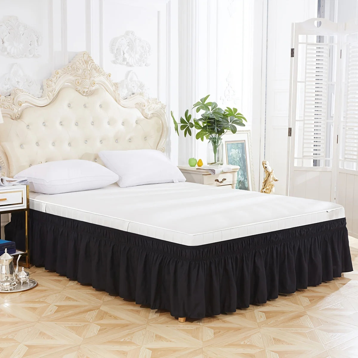 A white bed with a black ruffled skirt and white linens in a bright bedroom setting.