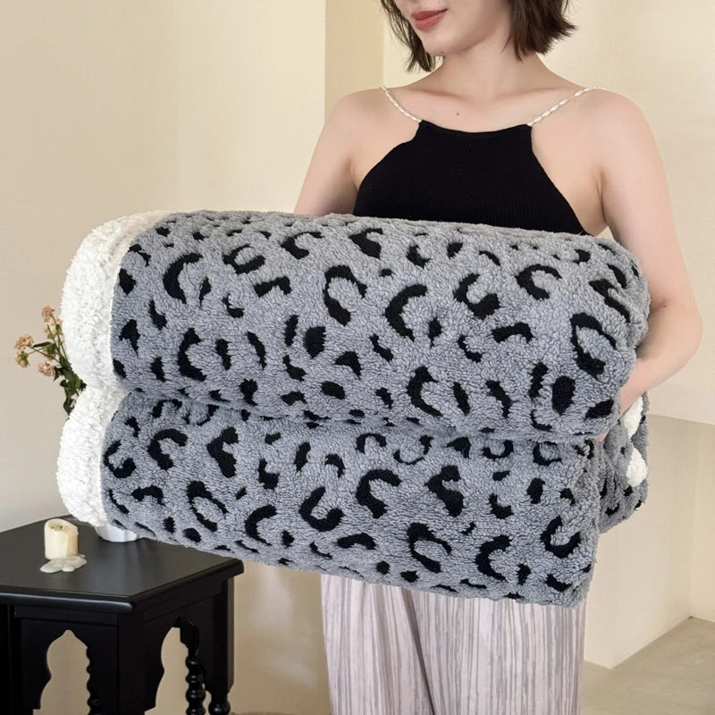 A woman holds a gray and black leopard print knit throw blanket against her chest.