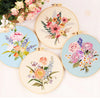 A collection of five embroidery hoops featuring various floral patterns in pink, purple, and orange threads on light fabric.