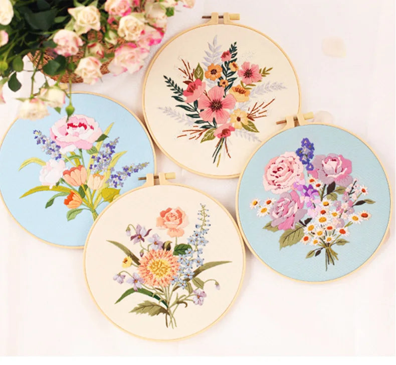 A collection of five embroidery hoops featuring various floral patterns in pink, purple, and orange threads on light fabric.