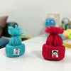 A close-up of two knitted yarn items, one teal and one red, featuring small face embroidery.