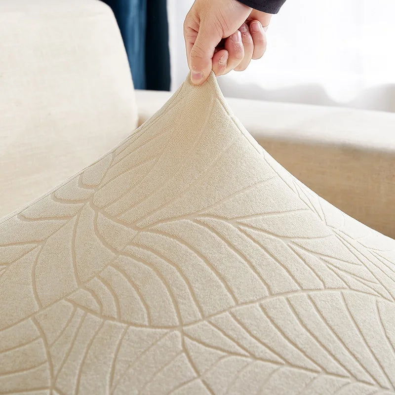 A hand is pulling the fabric of a beige waterproof jacquard stretch sofa cover.