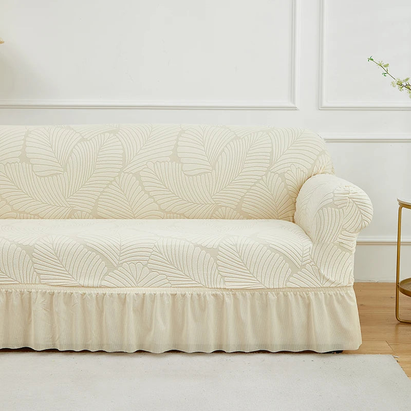 A cream jacquard stretch sofa cover featuring a leaf pattern displayed on a white sofa.