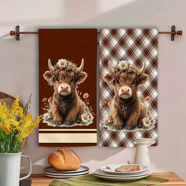 A set of two brown plaid kitchen towels featuring a cow motif, displayed on a wall.