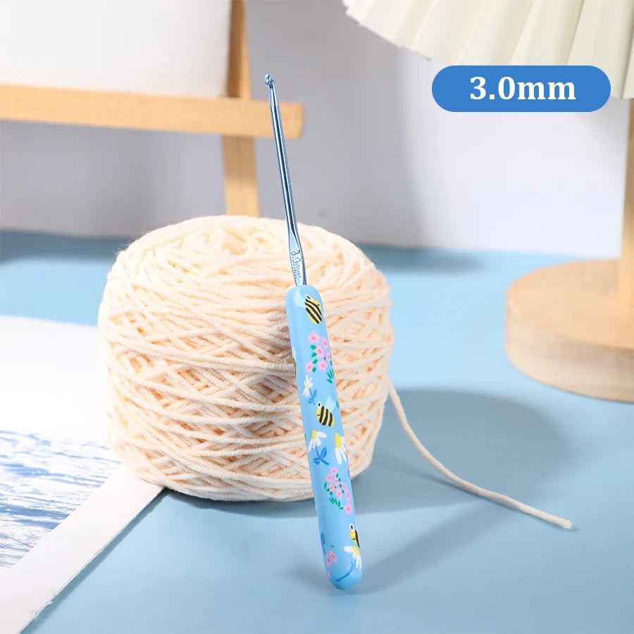 A blue ergonomic crochet hook with a thin wire is shown next to a ball of light pink yarn.