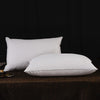 Two white natural goose down and feather sleeping pillows resting on a dark brown surface.