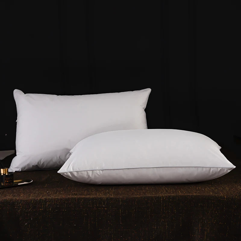 Two white natural goose down and feather sleeping pillows resting on a dark brown surface.