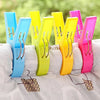 A pack of four large plastic clothes pins in various bright colors, including blue, yellow, and pink, resting on a white surf