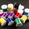 A collection of various colored elastic beading cords wound on spools and scattered on a dark surface.