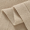 Close-up of a beige cotton baby swaddle blanket showing knitted texture and folded fabric.