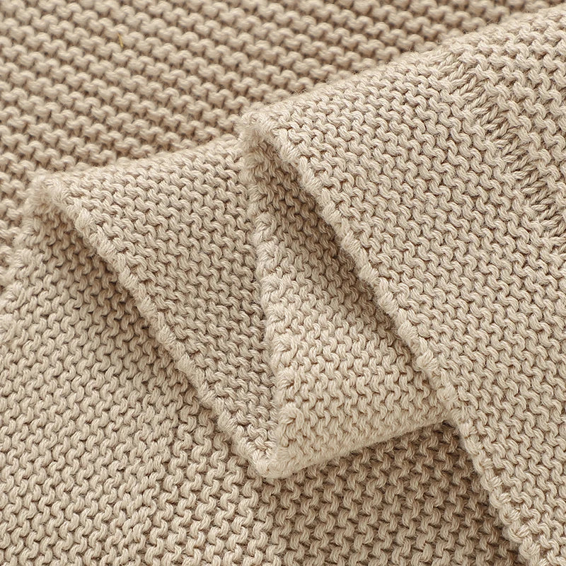 Close-up of a beige cotton baby swaddle blanket showing knitted texture and folded fabric.