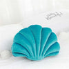 Teal velvet stuffed sofa cushion shaped like a decorative seashell on white bedding.