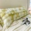 A fluffy, light green and white plush long pillow resting on a white textured blanket.