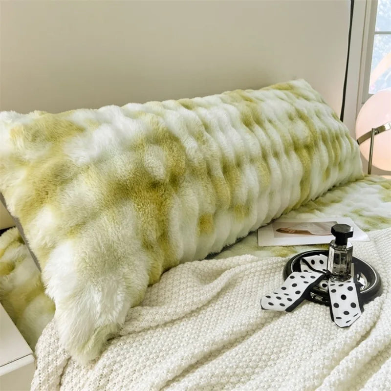 A fluffy, light green and white plush long pillow resting on a white textured blanket.