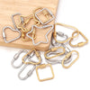 A collection of gold and silver heart-shaped screw lock carabiner clasps for jewelry making displayed on a wooden surface.