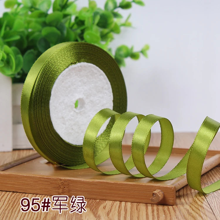 Roll of satin ribbon in olive green with white filling on a wooden surface