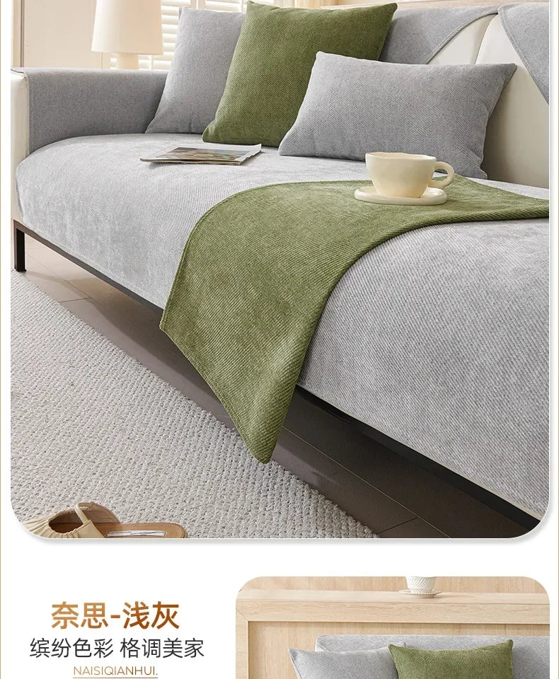 A light gray sofa is covered with a green protective fabric and features a white cup on the cover.