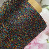 A close-up of multicolored glitter metallic yarn wound on a wooden spool.