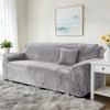 A gray stretch velvet sofa slipcover placed on a light rug in a bright room.