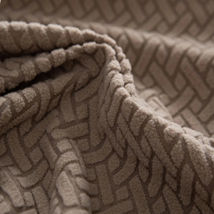 A close-up of a beige knitted fabric with a geometric pattern, likely a stretchy polar fleece sofa cover.