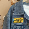 A close-up of a denim jacket showing an embroidered patch that reads There is nothing basic about me