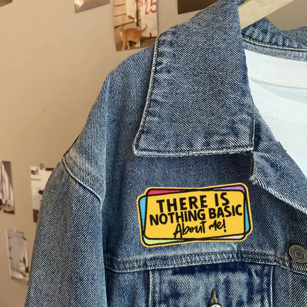 A close-up of a denim jacket showing an embroidered patch that reads There is nothing basic about me