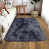 A plush solid black area rug placed on a wooden floor next to a bed.
