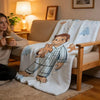 A white plush throw blanket featuring a C-Curious George character design draped over a light brown sofa.
