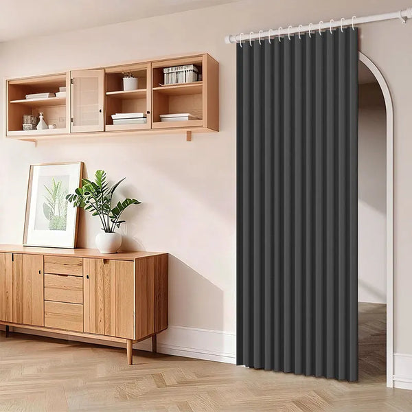 A dark gray pleated fabric door curtain hanging on a rod in a room with wooden shelving and cabinetry.