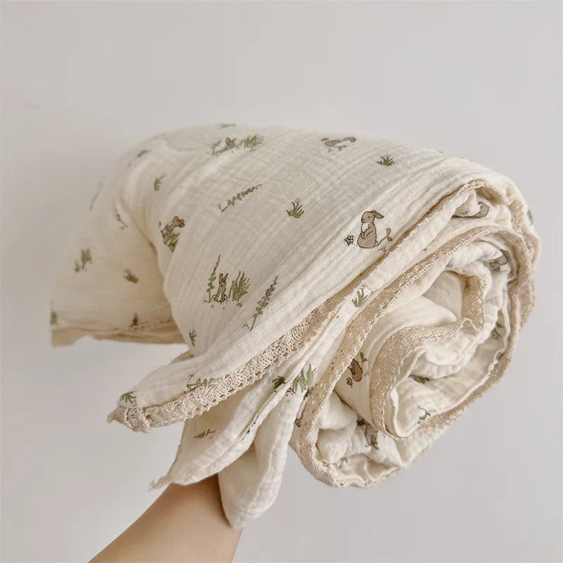 A rolled off-white muslin blanket with a subtle floral print featuring small animals, held by a hand.
