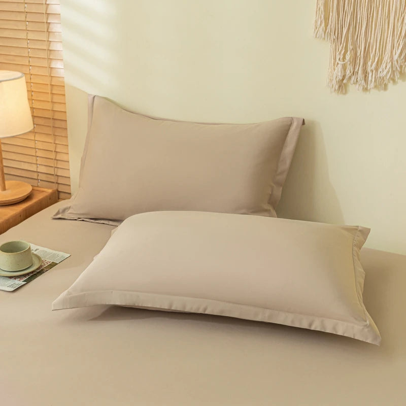 A set of solid beige fitted sheets and pillowcases displayed on a bed with natural light.
