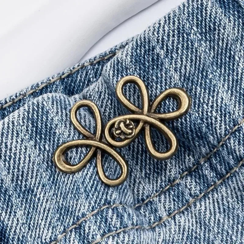 A gold-toned adjustable leaf clover waist tightener attached to a blue denim jean fabric.