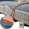 A close-up of a gray quilted sofa cover with orange trim and lace detailing, next to a silver washing machine.