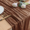 A brown cheesecloth table runner with draped folds, featuring white roses and gold cutlery on a wooden table.