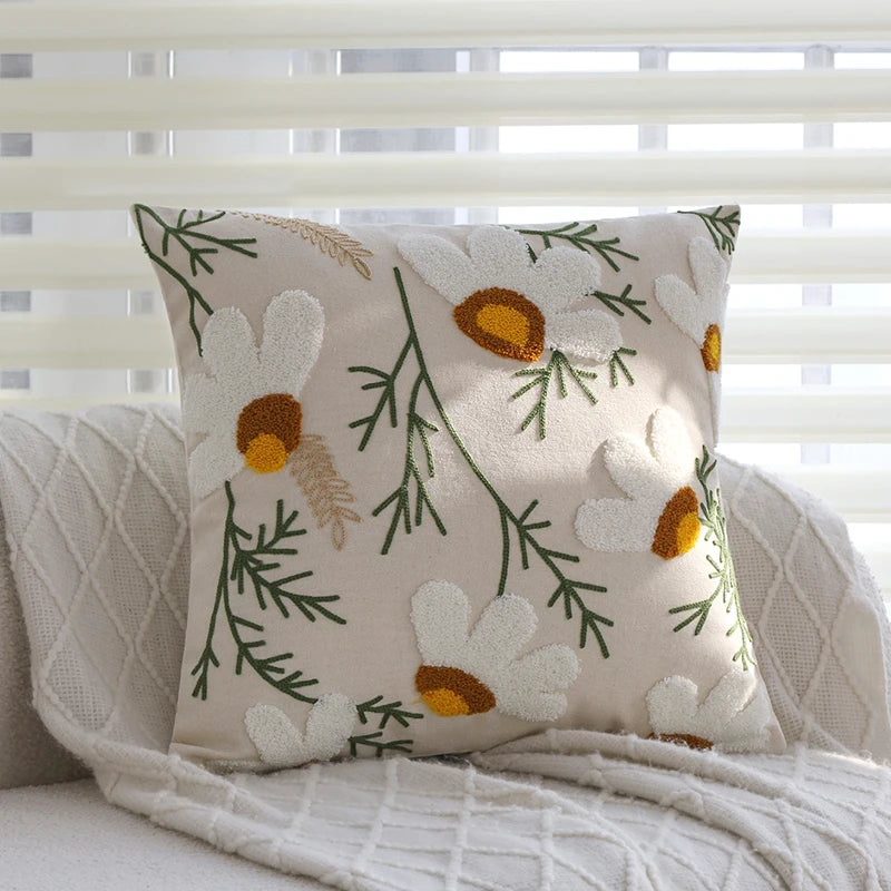 A beige cushion cover with embroidered white and yellow floral designs on a light-colored fabric.