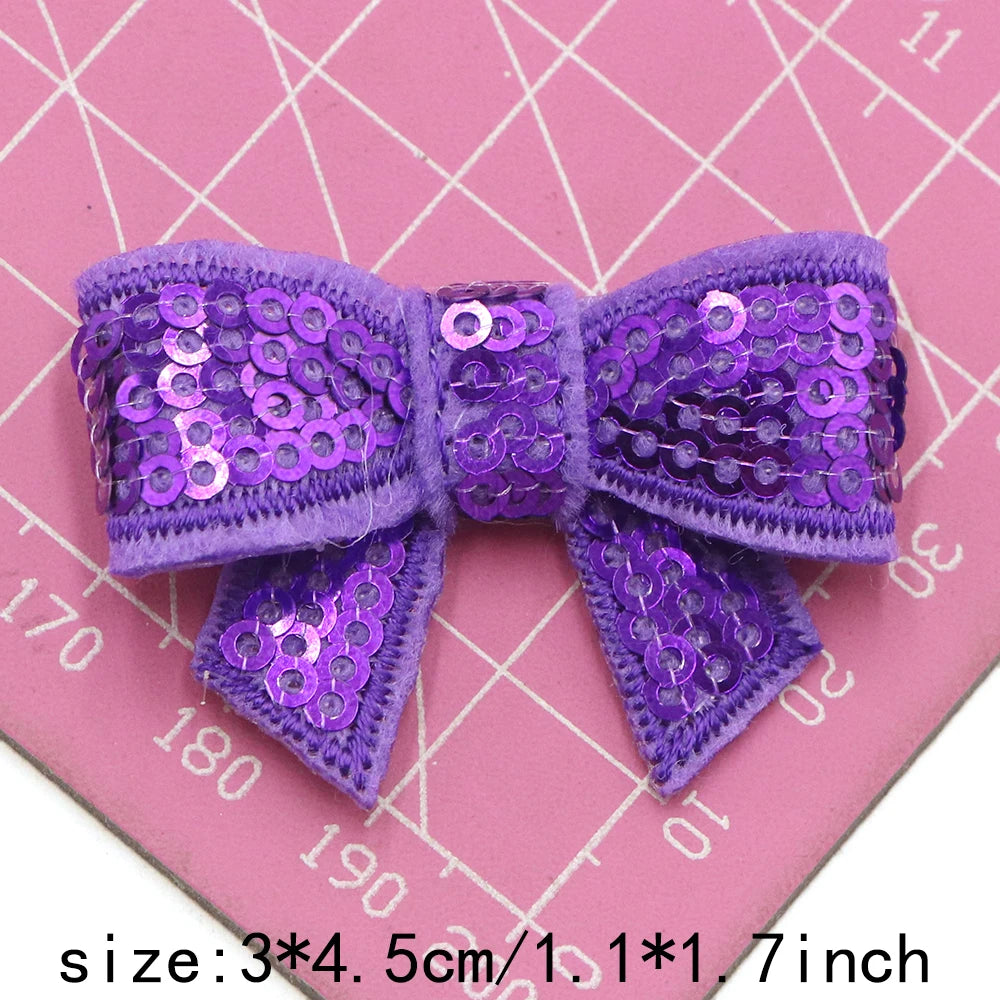 Purple sequin bow patches for DIY decoration shown on a pink grid background
