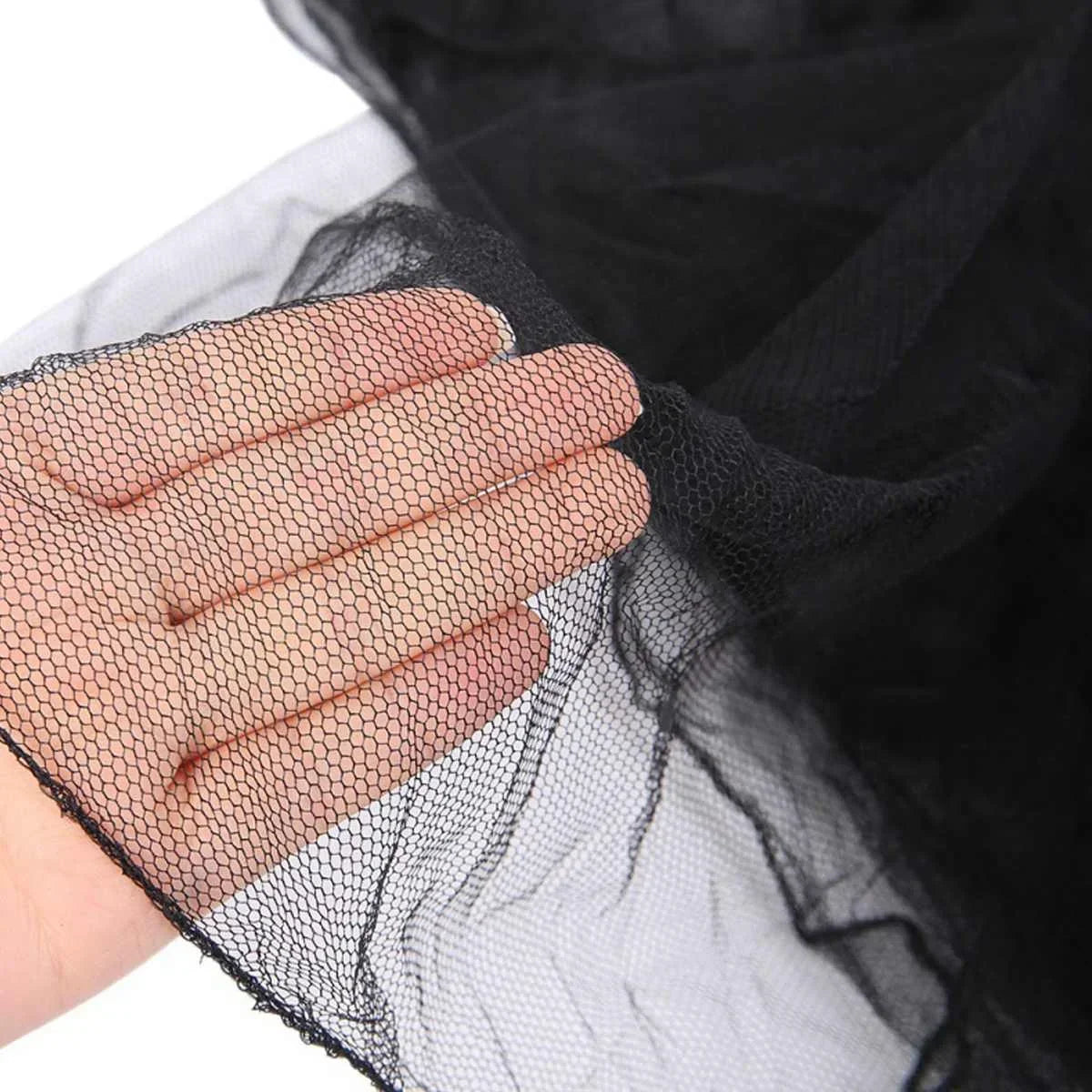 Close-up of a hand holding black mosquito netting fabric over a dark background.