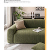 A green textured sofa cover with a beige cushion and a wooden coffee table in a bright living room setting.
