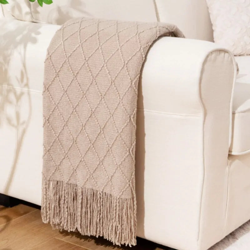 A beige knitted tassel throw blanket draped over a white leather sofa.