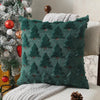 A dark teal knitted cushion cover with a repeating pine tree pattern resting on a light-colored sofa.