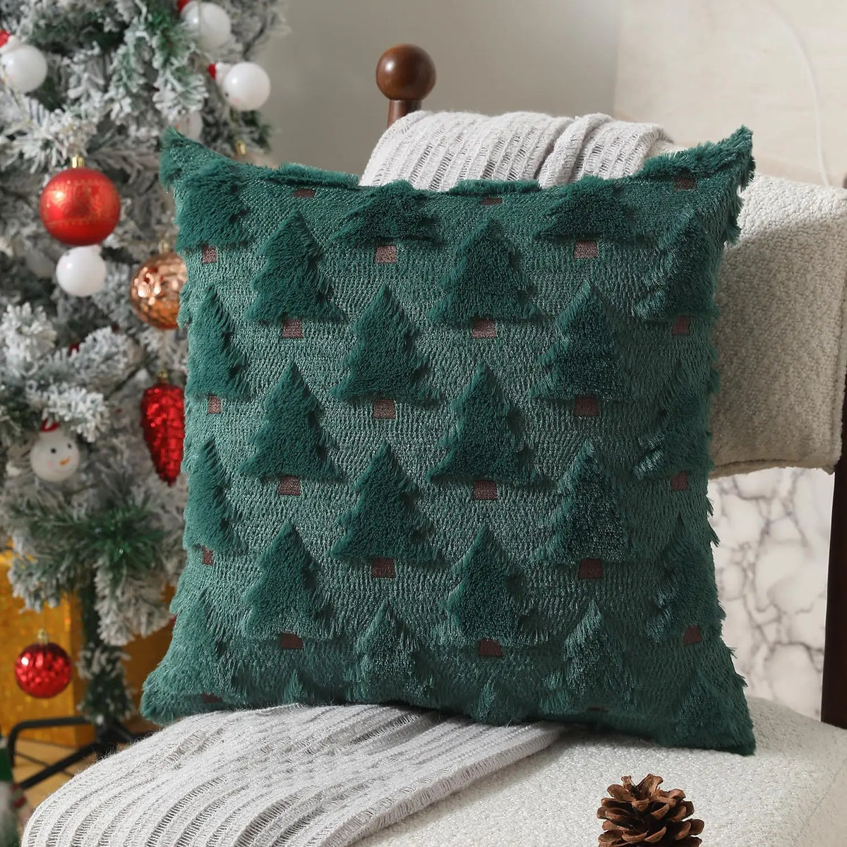 A dark teal knitted cushion cover with a repeating pine tree pattern resting on a light-colored sofa.