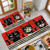 A rectangular red kitchen mat featuring a black cat print with white accents and black stripes.