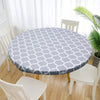 A round gray and white patterned vinyl tablecloth set on a wooden table surrounded by white chairs.